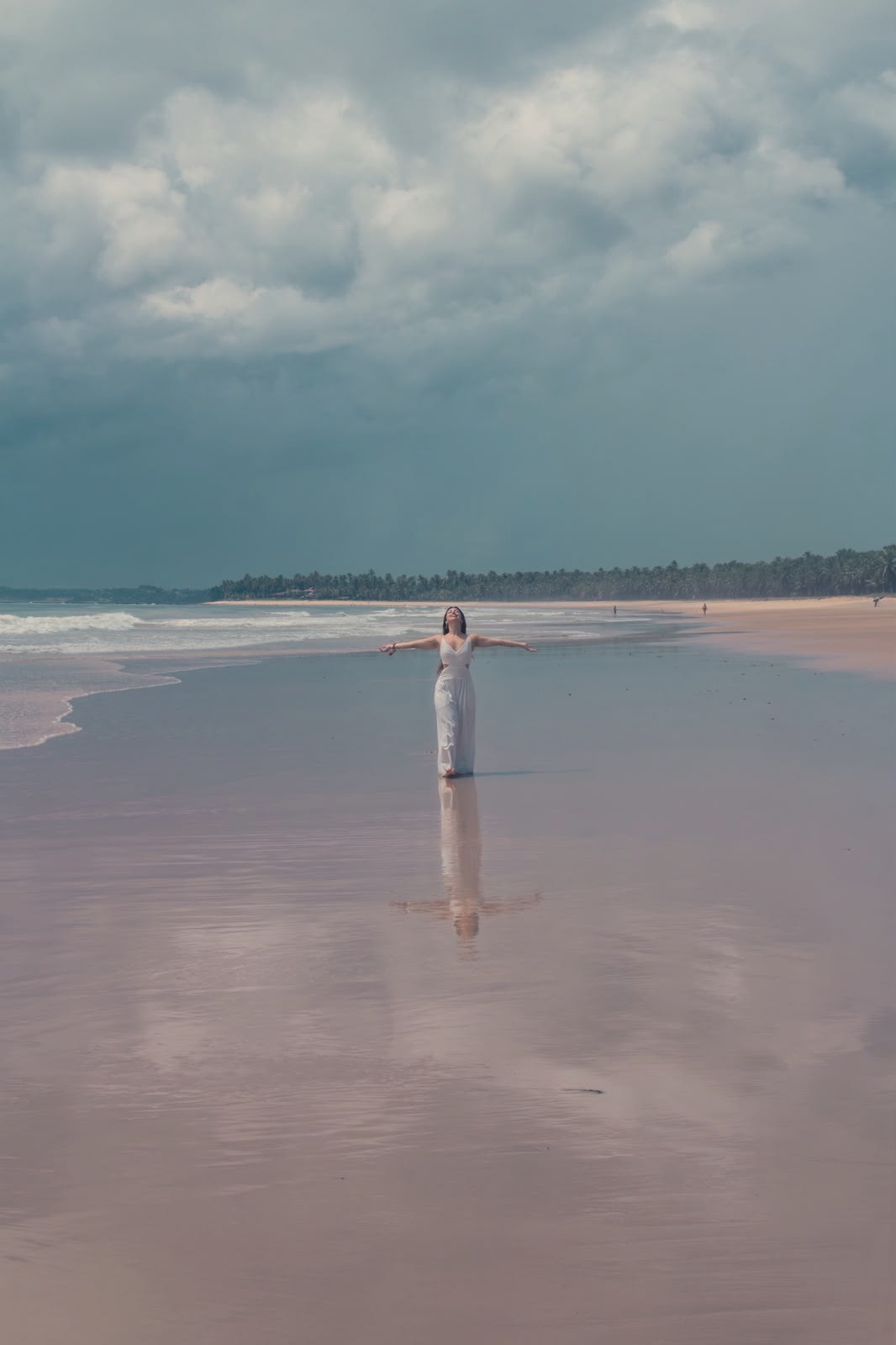 Madu pequena na imensidão da praia, de braços abertos, com o reflexo na areia molhada